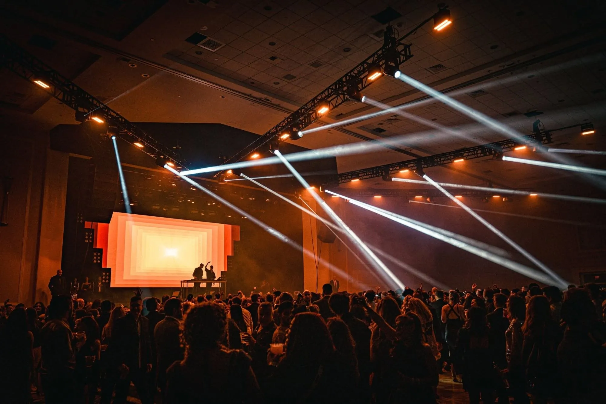 Big Night New Year’s Eve: a DJ duo plays in front of a glowing LED wall as light beams cut across the packed ballroom