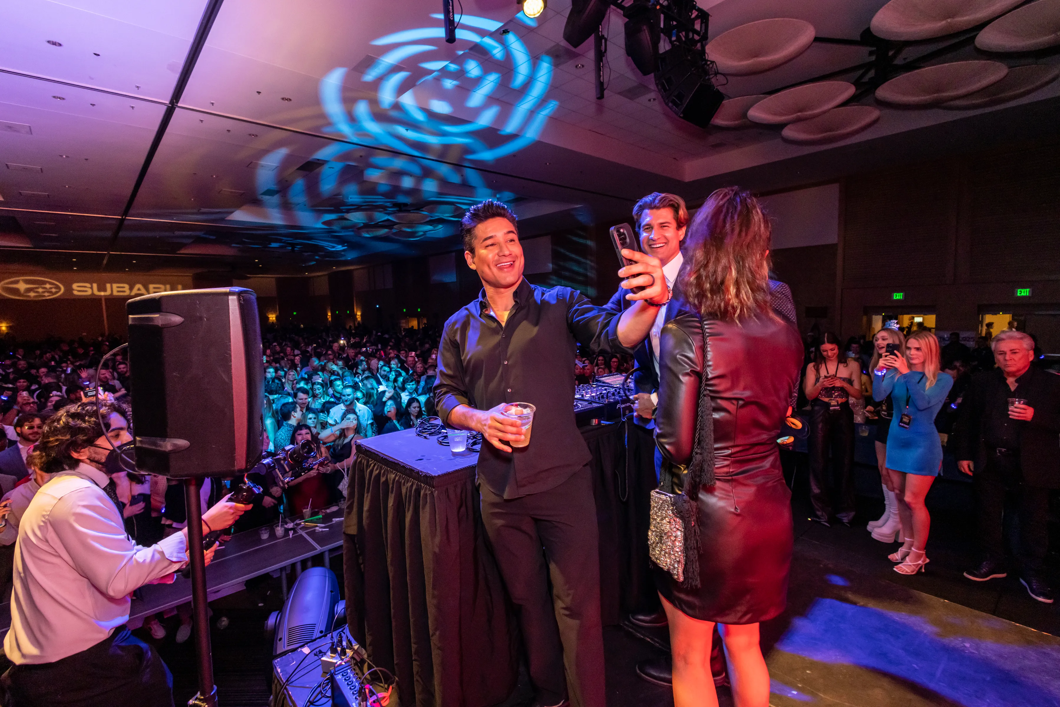 Mario Lopez takes a selfie with guests on stage at Big Night New Year’s Eve, a Subaru sponsor sign behind the crowd