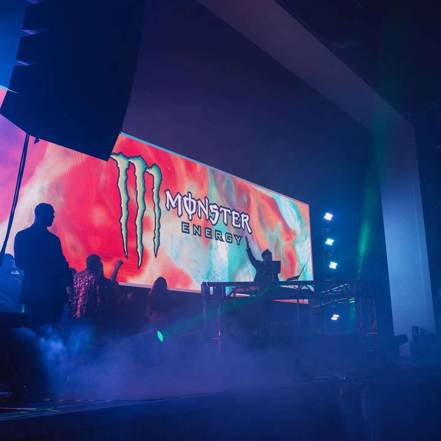 Monster Energy sponsor branding fills the LED wall behind the DJ booth at a HiBall Events stage, fog across the deck