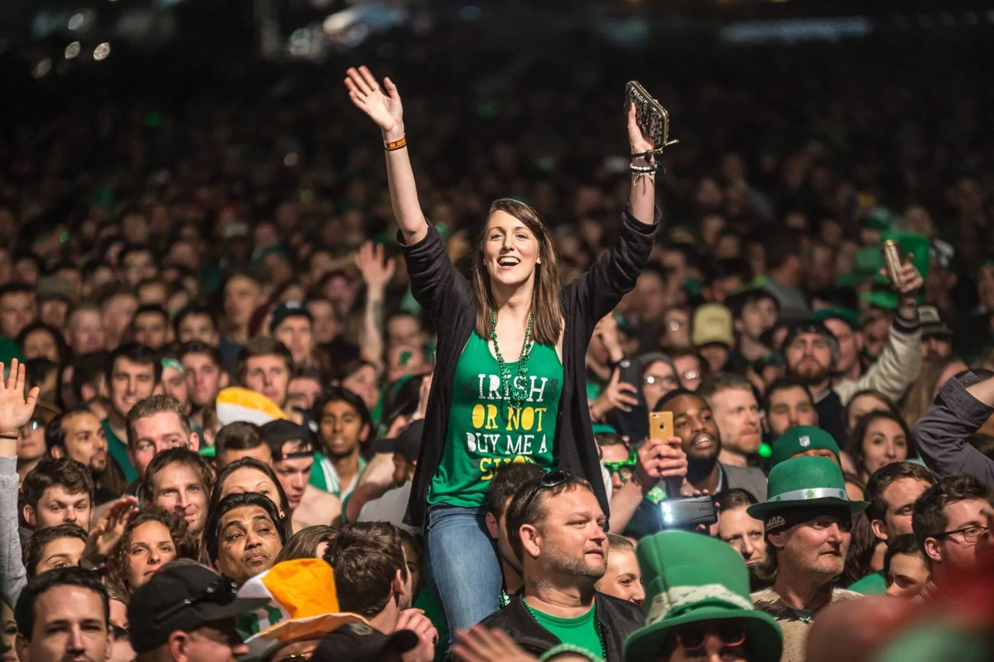 A ShamrockFest fan on someone’s shoulders waves above a packed crowd in green shirts and leprechaun hats