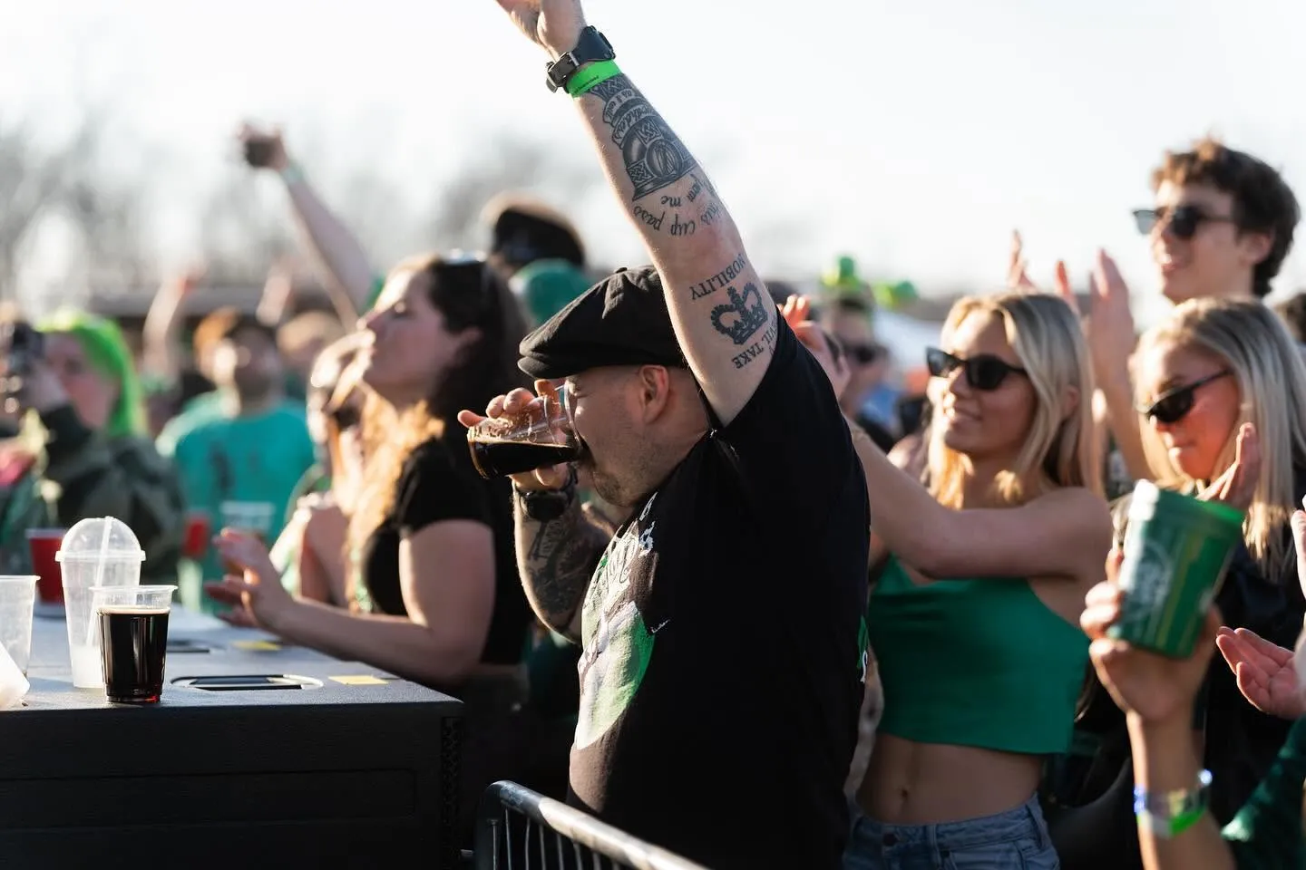 ShamrockFest fans in green cheer and raise a pint of stout at the front barrier of a stage