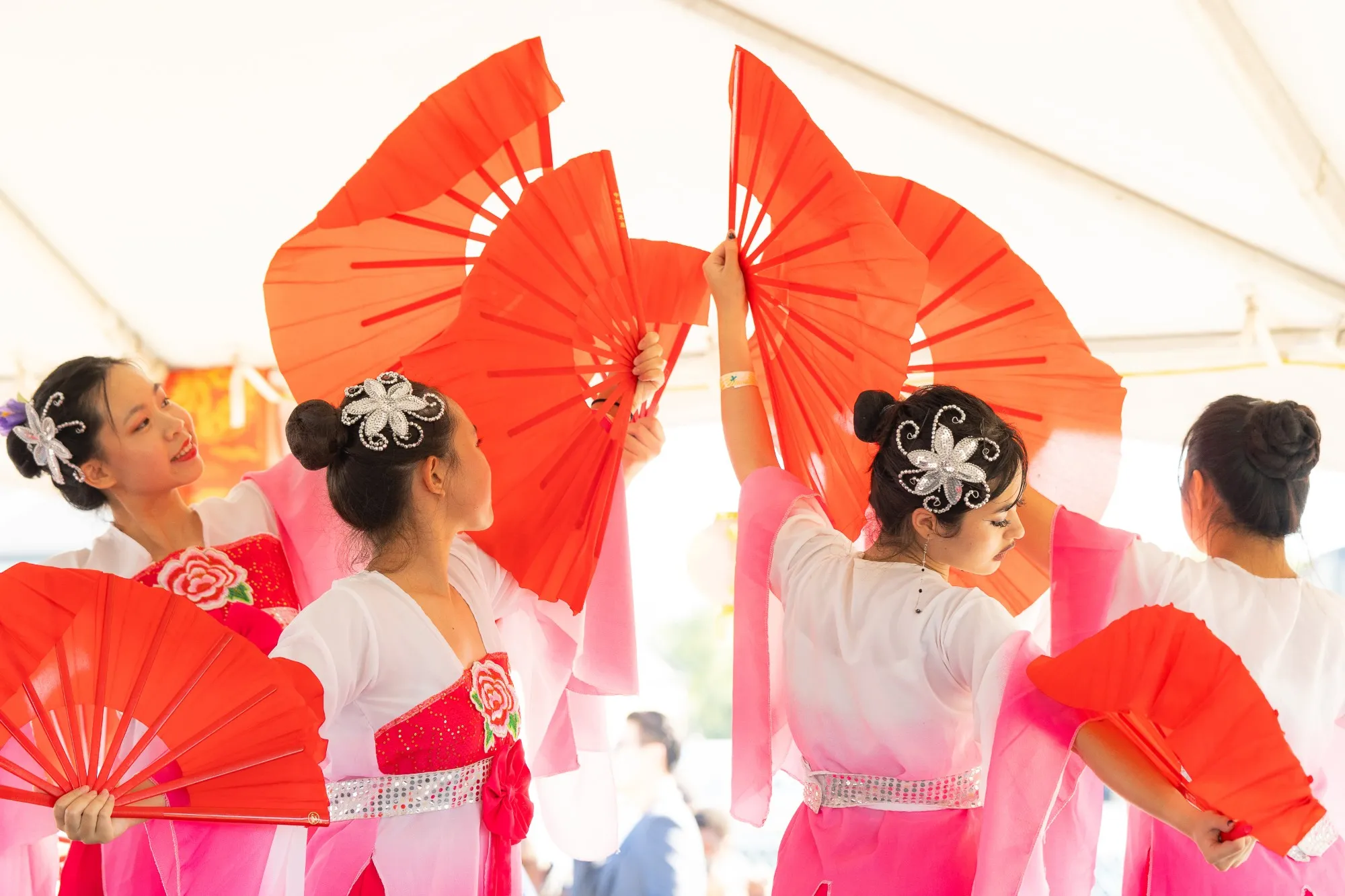 US Asian Fest in Loudoun County, Virginia: dancers in pink and white perform a Chinese fan dance with red fans on stage